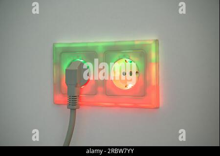 Rot und grün beleuchtete Buchse mit eingestecktem Stecker zur Darstellung des Stromverbrauchs und der elektrischen Energie aus einer Steckdose, die grüne Energie liefert Stockfoto