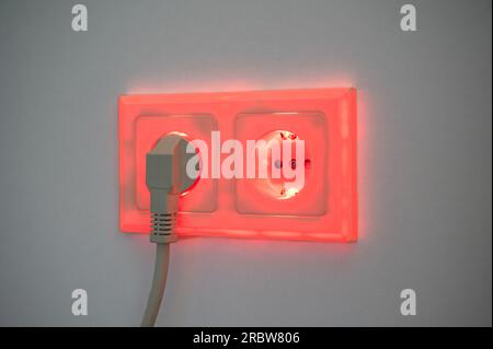 Rot beleuchtete Buchse mit eingestecktem Stecker zur Darstellung des Stromverbrauchs und der elektrischen Energie aus einer Steckdose Stockfoto