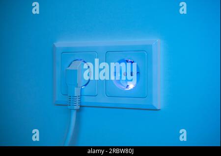 Blau beleuchtete Buchse mit eingestecktem Stecker zur Darstellung des Stromverbrauchs und der elektrischen Energie aus einer Steckdose Stockfoto