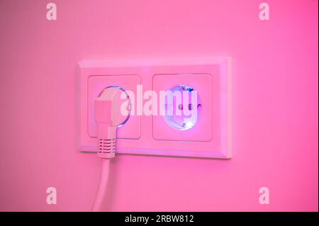 Blau und pink beleuchtete Buchse mit eingestecktem Stecker zur Darstellung des Stromverbrauchs und der elektrischen Energie aus einer Steckdose Stockfoto