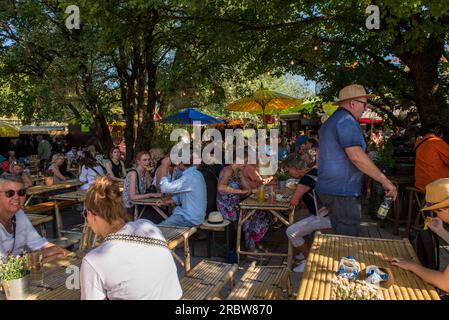 München, Deutschland - 7. Juli 2023: Auf dem Tollwood Festival der Stadt sitzen die Menschen in einem Biergarten Stockfoto