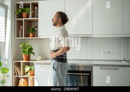 Junger Mann mit Lendenkorsett und Blick aus dem Fenster zu Hause Stockfoto