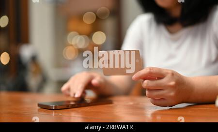 Nahaufnahme einer jungen asiatischen Frau, die eine Kreditkarte in der Hand hält und ihr Smartphone verwendet, um Online-Zahlungen in einer Shopping-App zu registrieren. Stockfoto