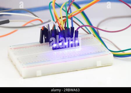 Blaues Licht, das von der SMD-LED oder einer parallel auf einer Steckplatine angeschlossenen Leuchtdiode ausgestrahlt wird. Leuchtende LED auf einer Steckplatine Stockfoto