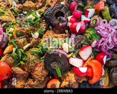 Schälen Sie Kebab mit Gemüse an der frischen Luft. Gegrilltes Fleisch mit frischen Tomaten, Zwiebeln, Radieschen und Kräutern Stockfoto