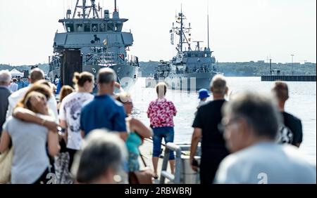 Kiel, Deutschland. 11. Juli 2023. Das Minenschiff "Bad Bevensen" (r) verlässt den Marinehafen von Kiel für einen Einsatz in einer der permanenten NATO-Minenabwehreinheiten. Zuschauer und Besatzungsmitglieder bleiben am Kai zurück. Kredit: Axel Heimken/dpa/Alamy Live News Stockfoto