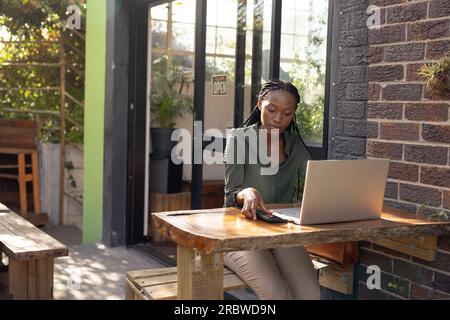 afroamerikanische Frau, die Laptop und Smartphone vor einem Café benutzt Stockfoto