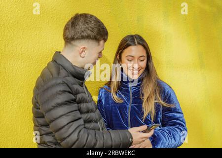 Ein lateinisches Mädchen, das mit einem Jungen auf gelbem Hintergrund chattet. Stockfoto