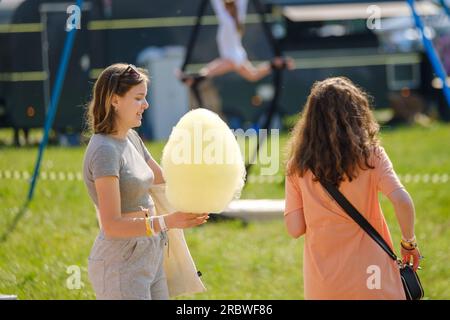 Moskau - 16. Juni 2023: Rückansicht einer anonymen Frau in legerer Kleidung, die mit einer Freundin auf dem Festival am sonnigen Sommer da steht und gelbe Zuckerwatte hält Stockfoto