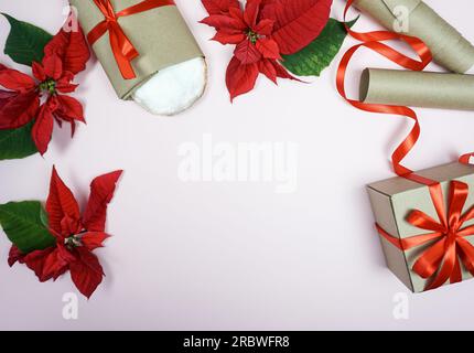 Auf rosafarbenem Hintergrund sind Gegenstände zum Feiern von Weihnachten angelegt: Ein Weihnachtsstollen, ein Geschenk, ein Poinsettia, ein Band zum Einpacken von Geschenken. Das Konzept von Weihnachten. Stockfoto