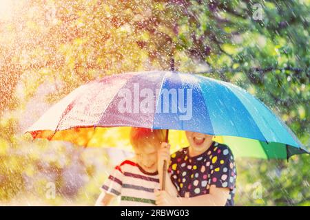 Junge und Mädchen stehen im Freien an regnerischen Tagen unter einem bunten Regenschirm. Stockfoto