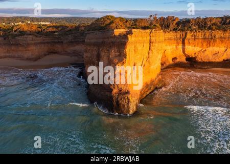 Aus der Vogelperspektive sehen Sie Wellen, die am Fuße der hohen Meeresklippen bei Anglesea auf der Great Ocean Road in Victoria, Australien, krachen Stockfoto