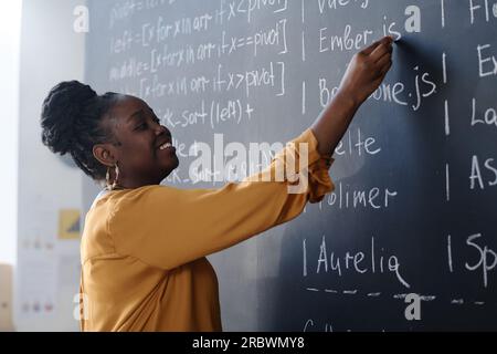Lächelnder afroamerikanischer Lehrer, der während des Unterrichts Formeln an der Tafel schreibt Stockfoto