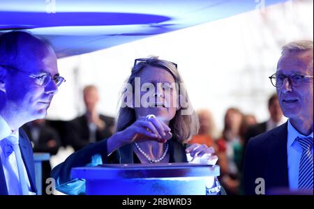 11. Juli 2023, Mecklenburg-Vorpommern, Warnemünde: Thomas Weigend (l-r), Geschäftsführer der Meyer Werft, Judith Pirscher, Staatssekretär im Bundesministerium für Bildung und Forschung BMBF, und Harald Fassmer, Geschäftsführer von Fassmer, legen bei der Kiellegezeremonie des Forschungsschiffs Meteor IV in der Neptun Werft traditionell eine Münze unter den Schiffsabschnitt. Das Bundesministerium für Forschung hatte den Bauauftrag an die Meyer-Werft in Niedersachsen, der die Neptun-Werft in Rostock angehört, und an Fassmer als Partner vergeben. Das A Stockfoto