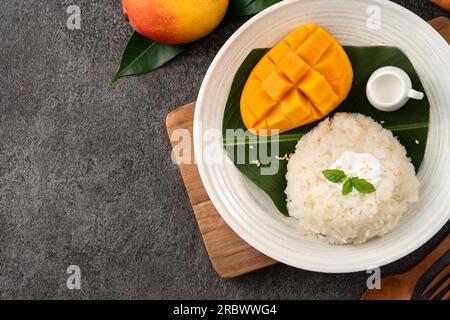 Köstlicher klebriger Reis aus thailändischer Mango mit geschnittenen frischen Mangofrüchten auf einem Teller mit grauem Tischhintergrund. Stockfoto