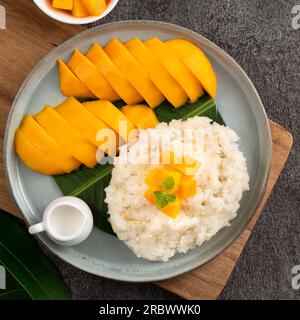 Köstlicher klebriger Reis aus thailändischer Mango mit geschnittenen frischen Mangofrüchten auf einem Teller mit grauem Tischhintergrund. Stockfoto