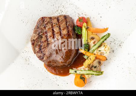 Gegrilltes Rinderfilet mit Demi-Glace-Sauce mit gegrilltem Gemüse auf einem weißen Porzellanteller Stockfoto