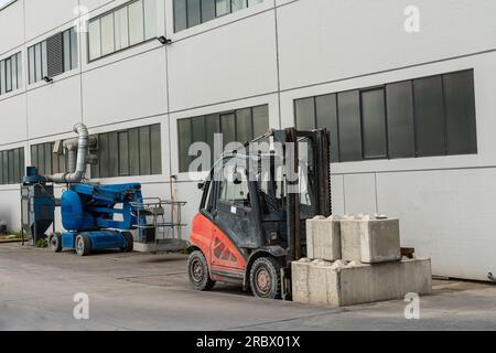 Ein kleiner Gabelstapler mit beladenen Betonblöcken steht in der Nähe des Gebäudes. In der Nähe des Aufzugs für Leute. Stockfoto