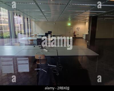 Leere Büroflächen mit Schreibtischen, Stühlen und Computermonitoren. Sonnenlicht kommt von den großen Fensterwänden an der Seite, keine Menschen, von außen gesehen. Stockfoto