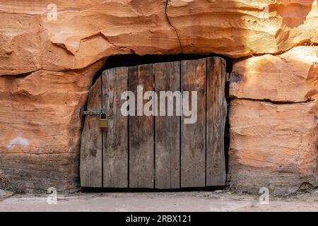 Raue Holztür mit Vorhängeschloss in orangefarbener Steinwand. Stockfoto