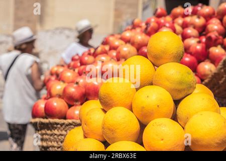 Orangen und Granatäpfel auf einem Straßenmarkt mit Kunden in verschwommenem Hintergrund Stockfoto