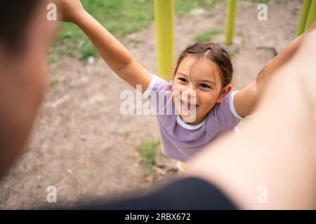 Kleine Tochter spielt mit Vater beim Workout im Fitnessraum im Freien. Fröhliche Gefühle. Gesunder Lebensstil in der Familie Stockfoto