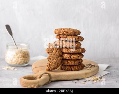 Gesunde Haferflocken-Kekse mit Datteln, Nüssen und Leinsamen auf einem Holzbrett auf grauem, strukturiertem Hintergrund. Köstliches hausgemachtes veganes Essen. Stockfoto