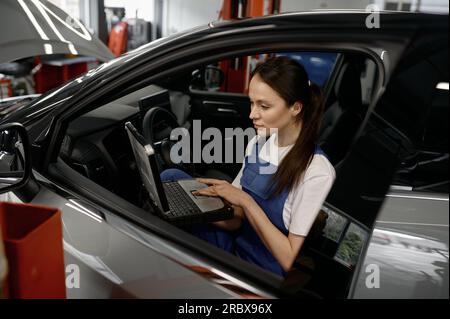 Frau, die im Auto sitzt und an einem Laptop arbeitet und Computerdiagnosen anbietet Stockfoto