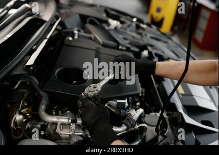 Schließen Sie die Hände eines Mechanikers mit einem Schraubenschlüssel unter der geöffneten Motorhaube Stockfoto
