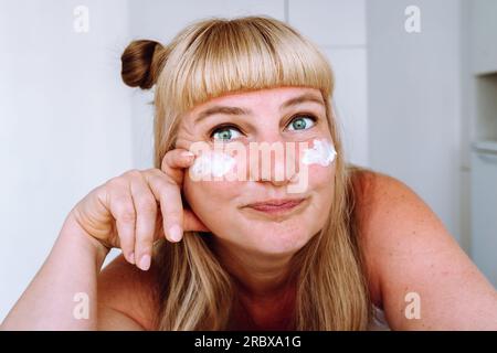 Porträt attraktive blonde Frau mittleren Alters mit kosmetischer Creme Stockfoto