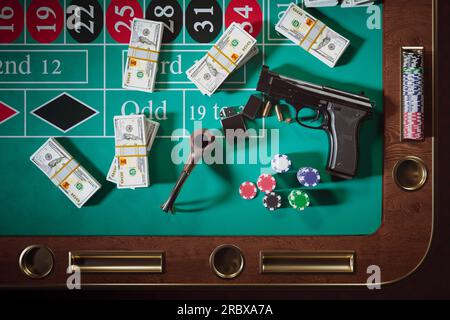 Waffen mit Kugeln, Geld und Chips auf einem Roulette-Tisch in einem Casino. Glücksspiel. Gangsterwaffe neben Geldbündeln, Pfeife mit Feuerstarter. Konzept von Stockfoto