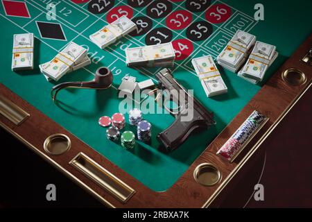 Waffen mit Kugeln, Geld und Chips auf einem Roulette-Tisch in einem Casino. Glücksspiel. Gangsterwaffe neben Geldbündeln, Pfeife mit Feuerstarter. Konzept von Stockfoto