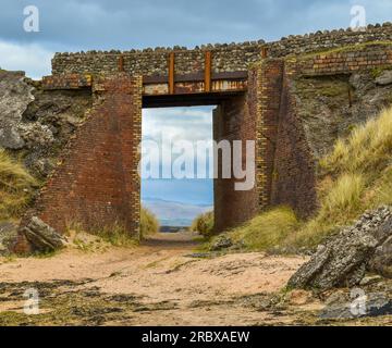 Eine alte Brücke am Strand mit einem sandigen Fußweg darunter. Stockfoto