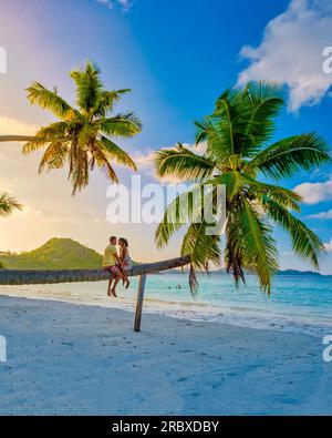 Praslin Seychellen tropische Insel mit weißen Stränden und Palmen, ein paar Männer und Frauen beobachten den Sonnenuntergang über einer Palme, die in einer Palme auf den Anse Volber Seychelles klettert. Stockfoto
