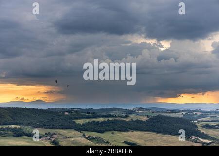 Sturmwolke aus der Ferne während des Sonnenuntergangs über der landwirtschaftlichen Landschaft in der Toskana, Italien Stockfoto