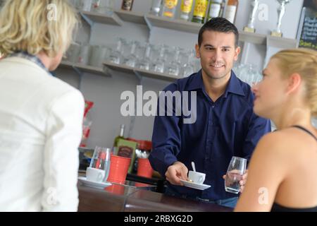 Angestellter in der Bar, der zwei weibliche Kunden bedient Stockfoto