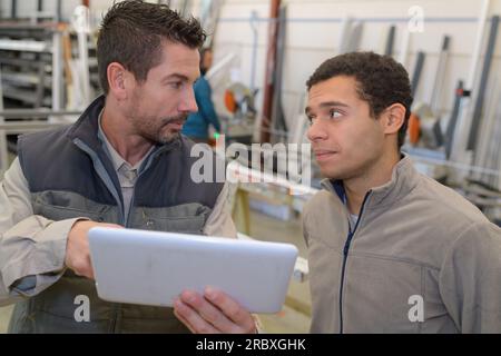 Fabrikarbeiter und Kollege, die in der Fabrik ein digitales Tablet verwenden Stockfoto