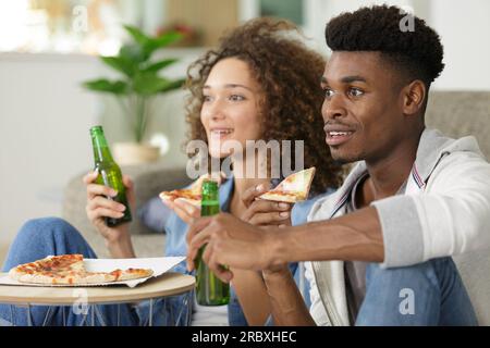 Ein Paar, das Sport im fernsehen sieht, während es Pizza isst Stockfoto