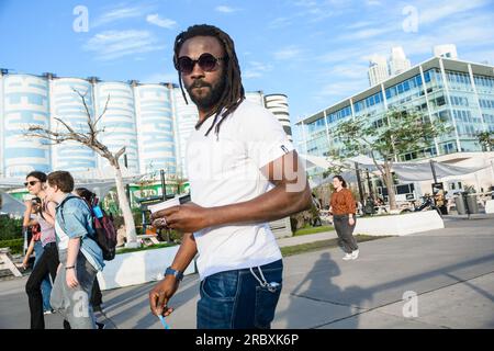 Ein junger Schwarzer mit Dreadlocks, der mit seinem überraschten Gesichtsausdruck in die Kamera schaut, läuft und isst draußen Eis, genießt den da Stockfoto