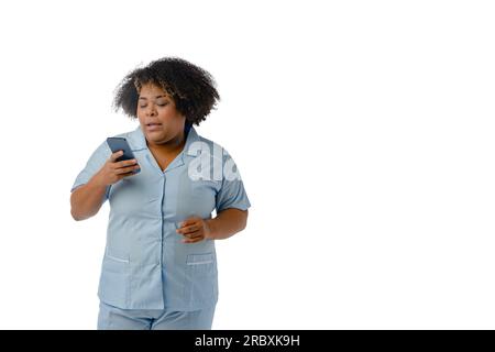 Junge afro-latinische medizinische Frau venezolanischer ethnischer Zugehörigkeit, die eine Nachricht auf ihrem Handy liest, weißer Hintergrund - Kopierraum, Kommunikation Stockfoto