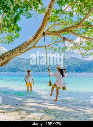Ein Paar spielt an einer Seilschaukel am Strand von Ko Ra WI Island Süd-Thailand, ein tropischer weißer Sandstrand mit türkisfarbenem Ozean im Tarutao National Park, Koh Rawi, Tambon Ko Tarutao Stockfoto