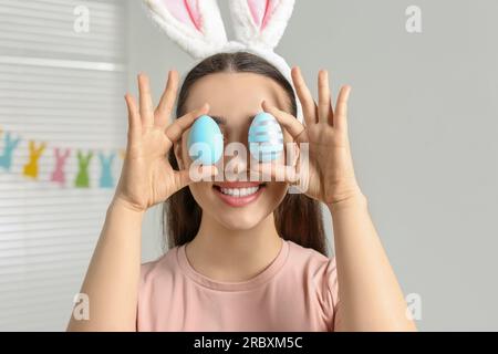 Glückliche Frau mit Hasenohren Stirnband, die bemalte Ostereier in der Nähe ihrer Augen hält Stockfoto