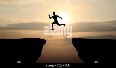 Konzept des Erreichens von Lebens- und Geschäftszielen. Silhouette eines Mannes, der bei Sonnenaufgang über die Schlucht springt Stockfoto