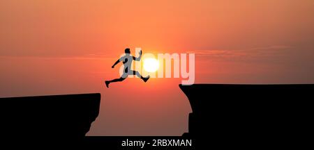 Konzept des Erreichens von Lebens- und Geschäftszielen. Silhouette eines Mannes, der bei Sonnenaufgang über die Schlucht springt Stockfoto