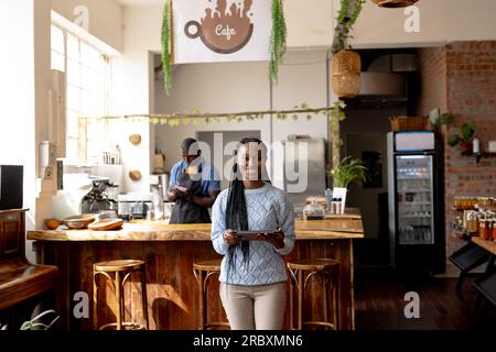 Porträt einer glücklichen afroamerikanischen Cafeterin, die ein Tablet gegen die Theke hält Stockfoto
