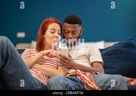 Junge, vielseitige Paare, die sich zu Hause mit dem Mobiltelefon ausruhen Stockfoto