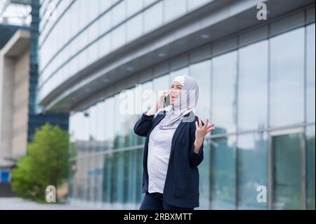 Schwangere Geschäftsfrau im Hijab und Anzug, die mit dem Smartphone spricht. Stockfoto