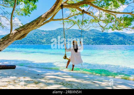 Eine Frau, die unter einem Baum schwingt, an einer Schaukel am Strand von Koh Lipe Island Süd-Thailand mit türkisfarbenem Meer und weißem Sandstrand bei Ko Lipe. Tarutao-Nationalpark, Insel Koh Rawi Stockfoto
