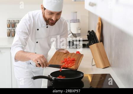 Glücklicher Koch, der im Haus geschnittene Tomaten in die Bratpfanne gab Stockfoto