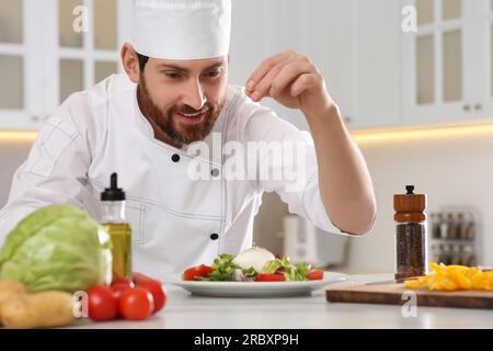 Professioneller Koch salzt köstlichen Salat am Marmortisch in der Küche Stockfoto